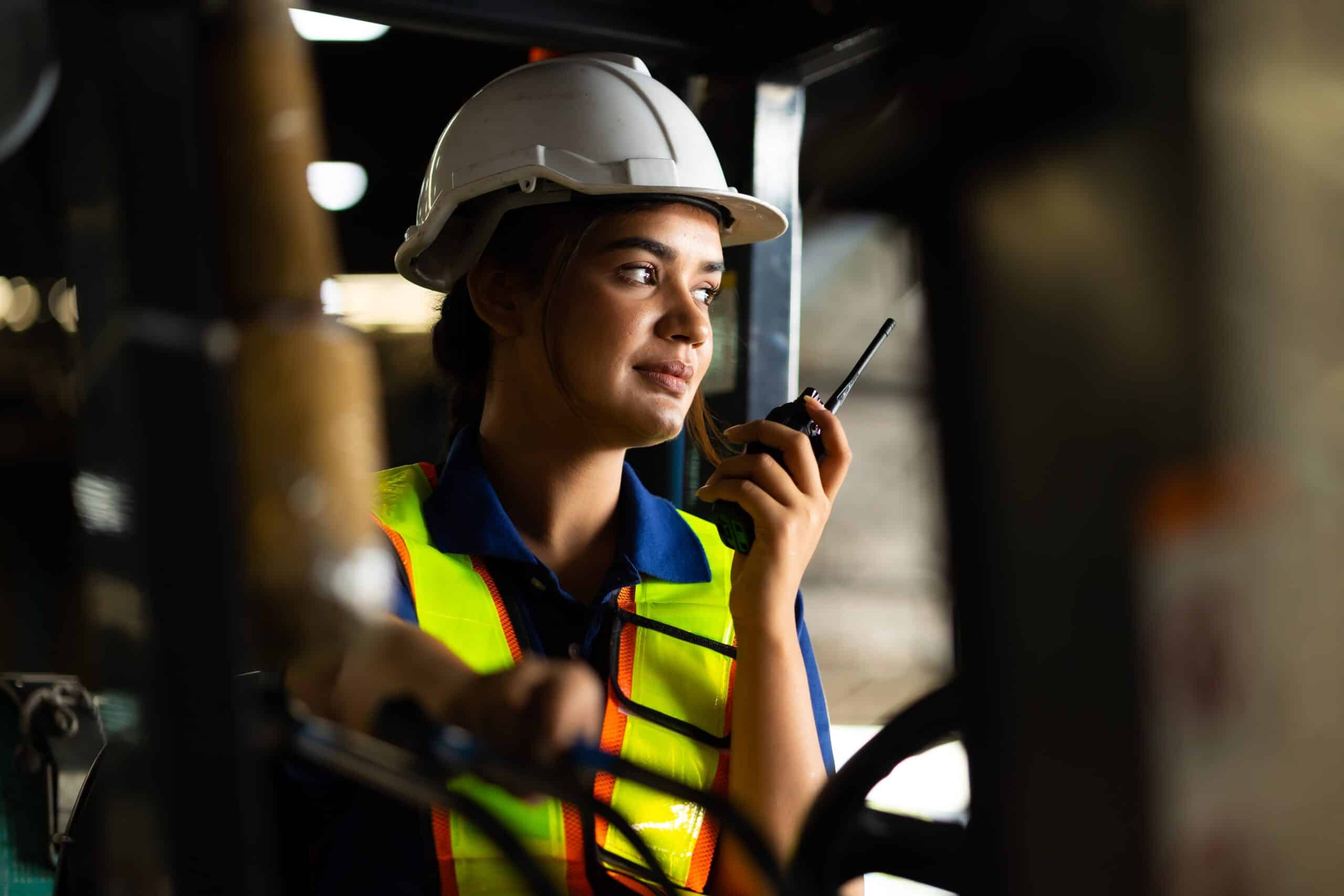 Jeune femme dans un environnement industriel tenant un walkie-talkie pour illustrer le dispositif de protection de travailleur isolé PTI